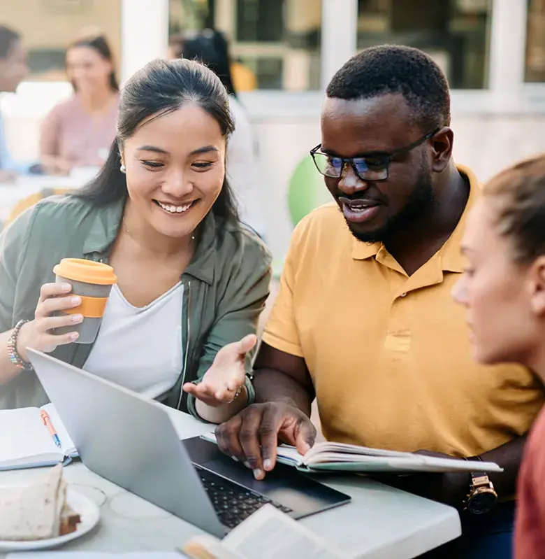 Three people in a university courtyard setting working on a laptop and drinking coffee